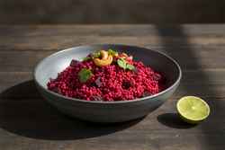 Vibrant magenta smoked beetroot and fonio pilau with toasted cashews in a rustic bowl. Minimalist African-inspired vegan gourmet culinary photography.