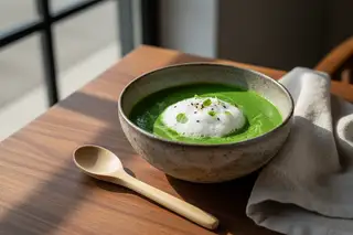 Minimalist Moringa coconut broth with airy foam and microgreens in a ceramic bowl on a dark teak table. Elegant Afro-Asian plant-based dish.