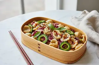 Modern bento: orecchiette in miso-walnut cream, purple radicchio, bitter melon, and chili oil. Sleek chopsticks on a light marble surface.