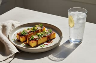 Crispy miso polenta bites with radish & zest beside a sparkling ginger drink. Elegant Mediterranean-Asian fusion on a sun-drenched stone table.