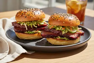 Two Gochujang seitan brisket sliders with miso slaw and sesame seeds on a minimalist plate, bathed in bright California sunlight.