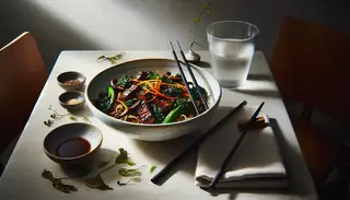 Image of a vegan umami dish with seitan and mushrooms in a white bowl, served with chopsticks and water, set on a minimalist table.
