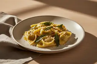 Miso-roasted fennel agnolotti with ginger-sage glaze and shichimi togarashi on a minimalist plate in soft, natural Mediterranean light.