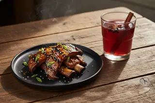 Smoky pomegranate-glazed King Oyster mushroom ribs with a spiced garnet mocktail on a rustic wood table in warm golden-hour light.