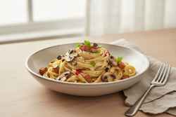 Smoky Miso & Black Garlic Mushroom Carbonara Gourmet vegan miso carbonara with linguine, shiitake, tempeh bacon, and black garlic, drizzled with chili oil in a minimalist ceramic bowl.