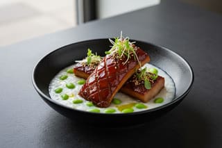 Glazed Char Siu King Oyster 'bone marrow' over creamy truffle edamame congee in a matte black bowl, garnished with micro-shiso.