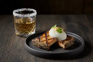 Wood-fired King Oyster mushrooms with sesame crust and yuzu foam, paired with a botanical infusion on a minimalist, Zen-inspired table.