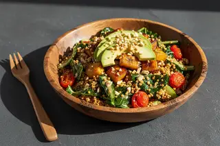 Vegan Serengeti Sizzle: Crispy millet, plantains, and avocado in a rustic wooden bowl on a dark stone surface. Soft natural lighting.