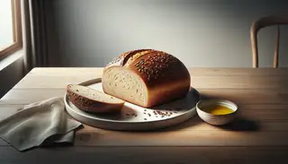 Freshly baked bread with a golden-brown crust, cut open on a white plate, beside a bowl of olive oil, on a wooden table under natural light.