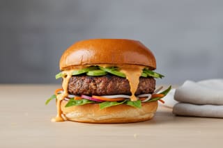 Gourmet vegan burger: mushroom-walnut patty, gochujang cream, pickled daikon and Thai basil on a golden brioche bun. Minimalist food photography.