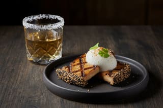 Wood-fired King Oyster mushrooms with sesame crust and yuzu foam, paired with a botanical infusion on a minimalist, Zen-inspired table.