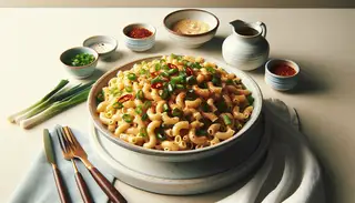 Heaping dish of Asian-inspired vegan mac and cheese with green onions and chili flakes, on a minimalistic white and silver table setting.