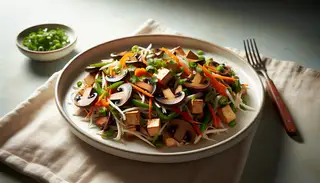 Vegan shredded mushroom and tofu stir-fry on a white plate, garnished with cilantro and green onions, in natural light on a minimalist table.
