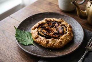 Koji-Aged Pastry with Binchotan Kabocha A rustic fermented rice-flour pastry with charred kabocha squash on a dark wabi-sabi ceramic plate.