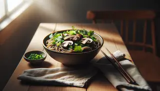 A cozy bowl of Vegan Miso Mushroom Soba on a wooden table, with mushrooms, onion, cilantro, chopsticks, and a napkin under soft light.