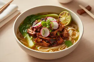 Golden Yuzu-Ginger BBQ Soup topped with charred jackfruit and fresh herbs on a sunlit wooden table. Minimalist vegan Asian-American fusion.
